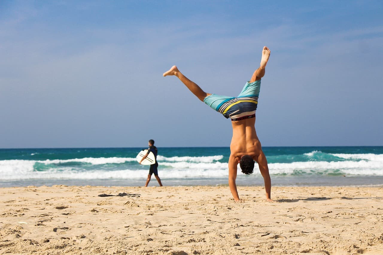 man doing a handstand at the beach